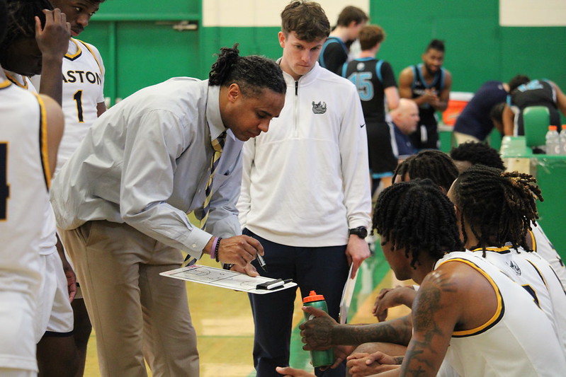 Gaston College interim head coach Jermaine Williams (leaning over) plots strategy for the Rhinos during Sunday's game at Gastonia's Ashbrook High School.